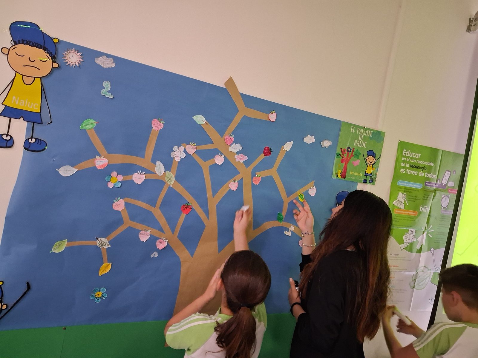 Varios alumnos colocan figuras recortadas en el mural del aula durante una sesi&oacute;n.