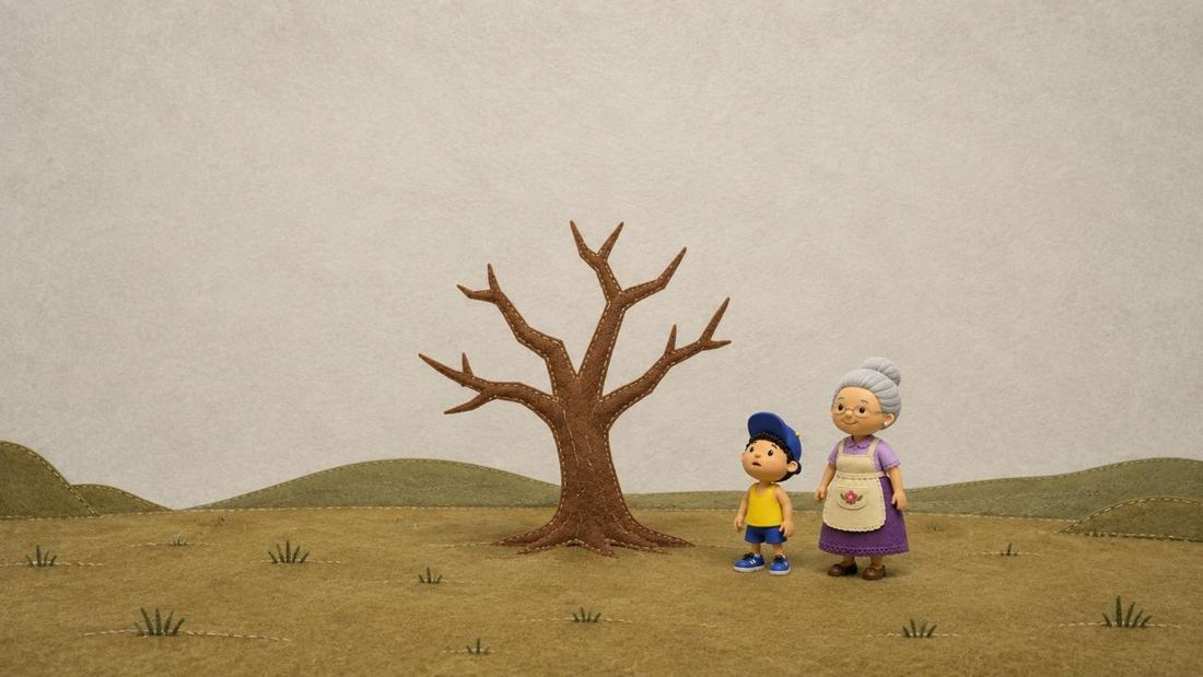 Un campo vacío con un árbol de fieltro pelado. Naluc y su abuela lo miran.